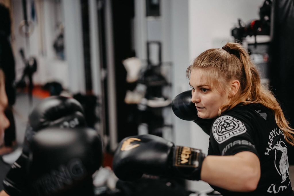 Fokussierte Trainerin von Harrycane Luta Livre beim Boxtraining mit schwarzen Handschuhen im Trainingsraum.