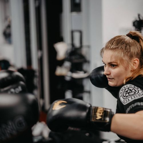 Fokussierte Trainerin von Harrycane Luta Livre beim Boxtraining mit schwarzen Handschuhen im Trainingsraum.