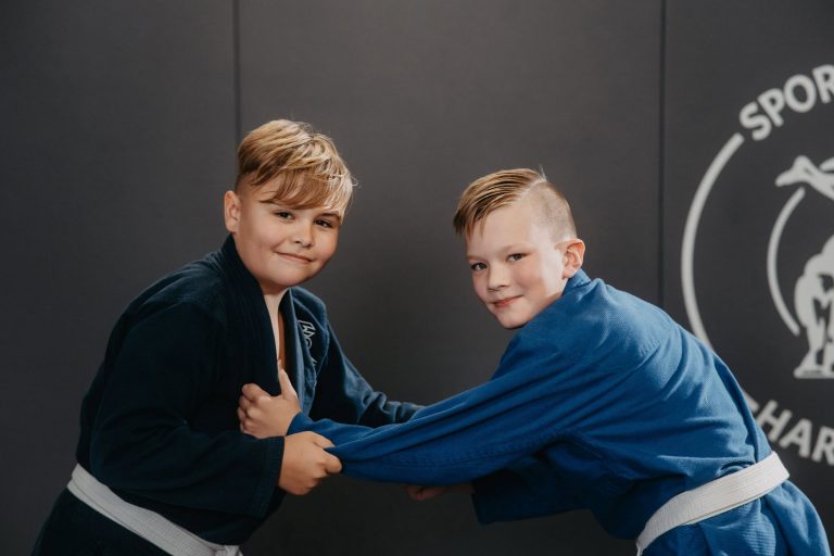 Über uns 9 Zwei Jungen im Kindertraining bei Harrycane Luta Livre, üben Grifftechniken in blauen Gi-Trainingsanzügen.