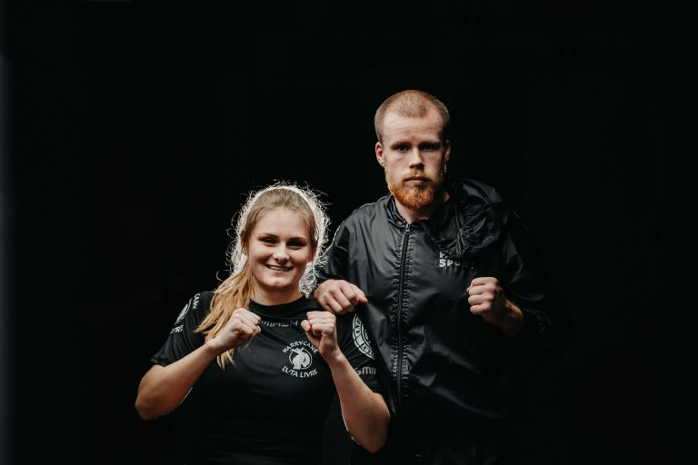 Über uns 14 Mitglieder von Harrycane Luta Livre in schwarzer Trainingskleidung, motiviert in Kampfhaltung vor dunklem Hintergrund.