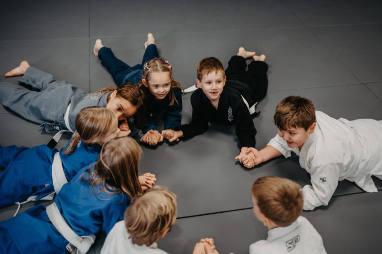 Über uns 15 Kinder liegen im Kreis auf der Matte und halten sich an den Händen, symbolisch für das familiäre Umfeld in der Sportschule Harrycane in Herford.